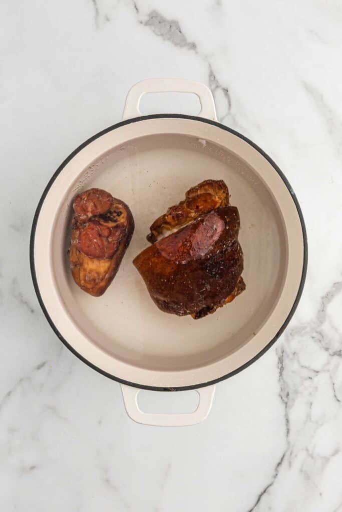 Ham hocks in the pot to with water on white countertop