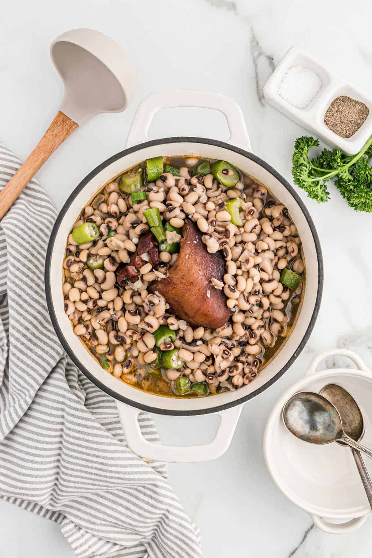 Southern black eyed peas with ham hocks in a pot on the table with a spoon next to it to serve.