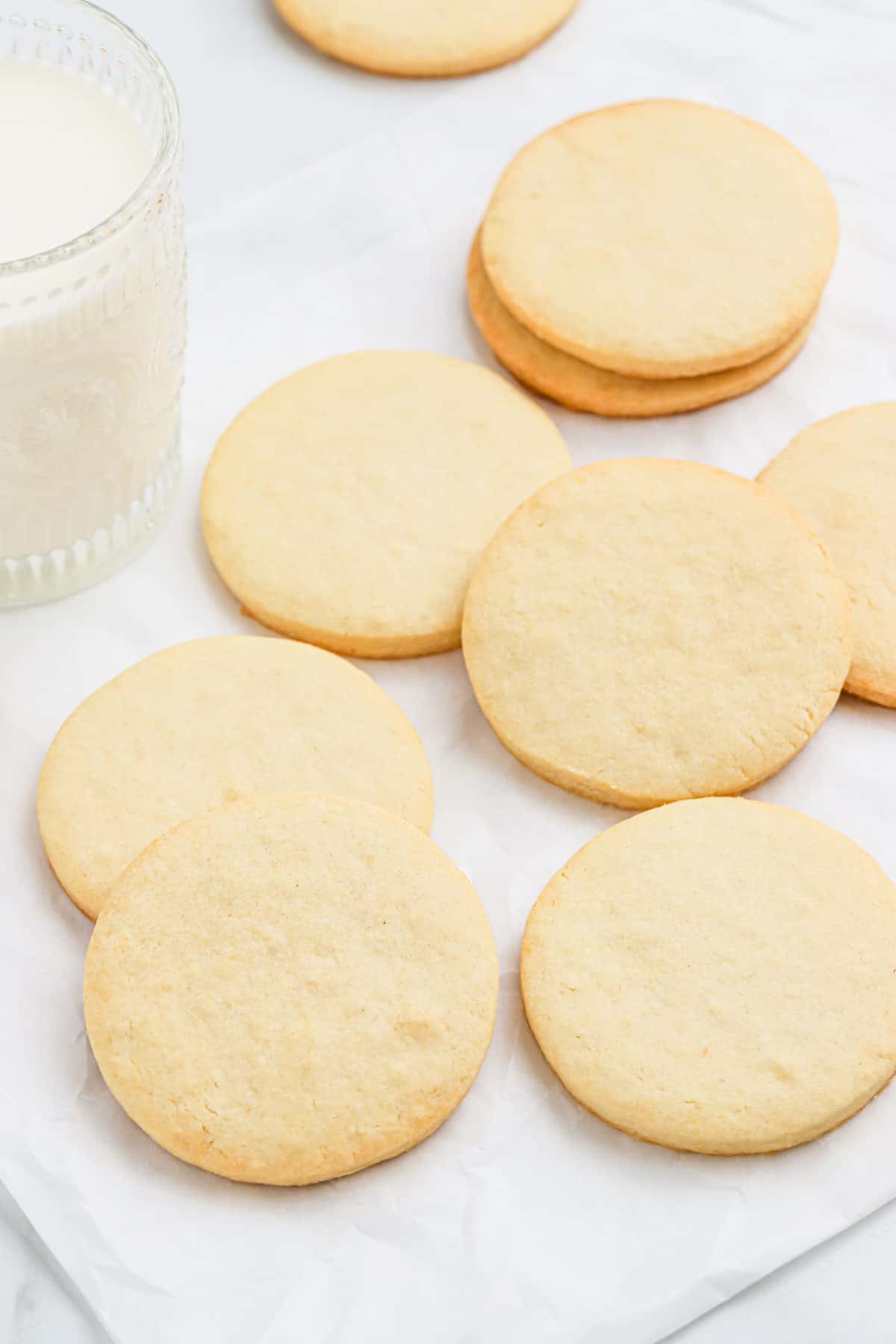 Plain sugar cookies on the table with a glass of milk.