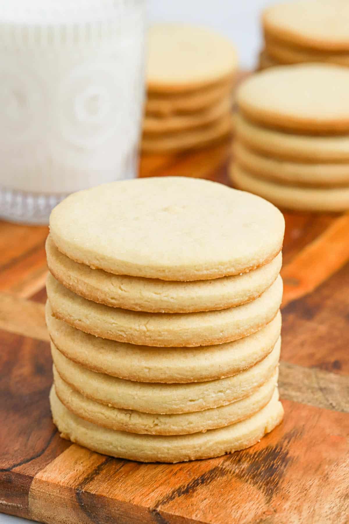 A stack of round sugar cookies without icing in front of milk.