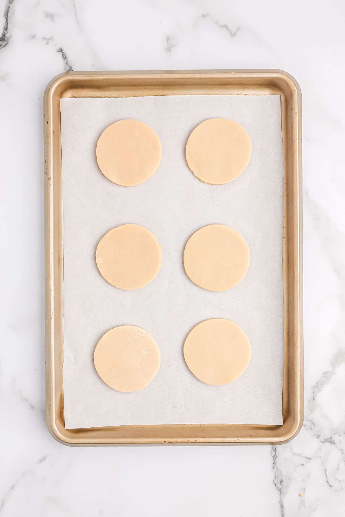 Rolled sugar cookies cut into circles on a baking sheet.