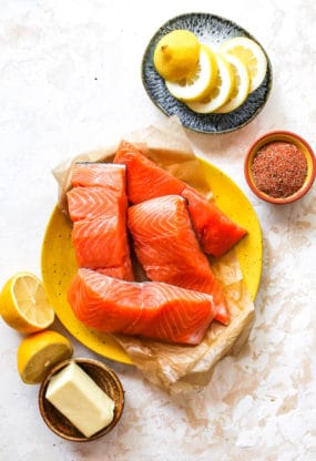 Fresh salmon fillets on a yellow plate with lemon wedges around