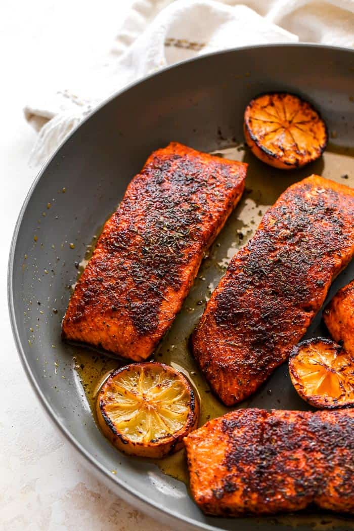 Seared salmon with cajun spice in a pan with lemon wedges