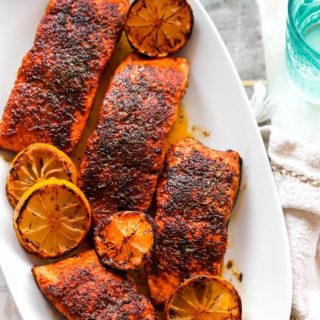 A delicious white platter filled with blackened salmon fillets with lemon wedges