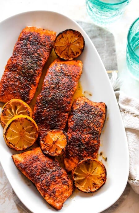 A delicious white platter filled with blackened salmon fillets with lemon wedges