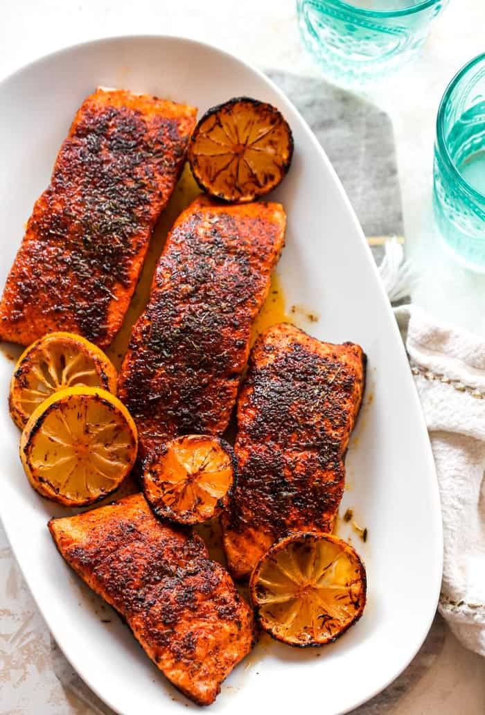 A delicious white platter filled with blackened salmon fillets with lemon wedges