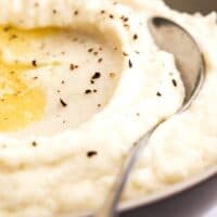 A close up of creamy cauliflower grits with butter melted over it and sprinkles of pepper ready to serve