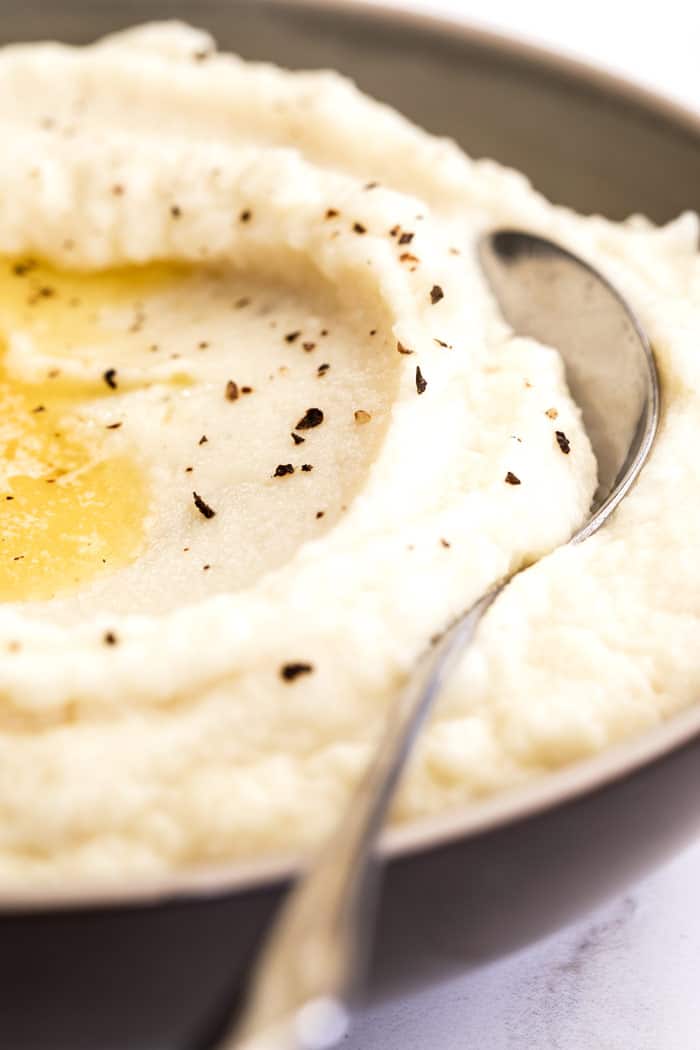 A close up of creamy cauliflower grits with butter melted over it and sprinkles of pepper ready to serve