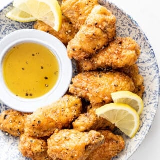 Delicious lemon pepper wings scattered on serving plate with lemon glaze on side for dipping