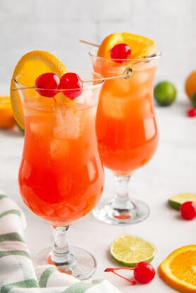 Two hurricane cocktails ready to serve with limes, cherries and orange slices around