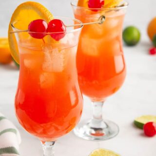 Two hurricane cocktails ready to serve with limes, cherries and orange slices around