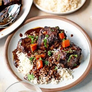 A close up of a white plate with oxtails and white rice ready to serve