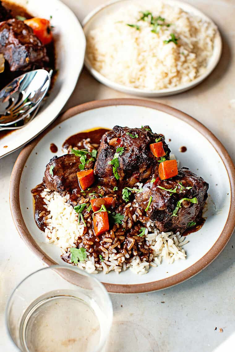 A close up of a white plate with oxtails and white rice ready to serve