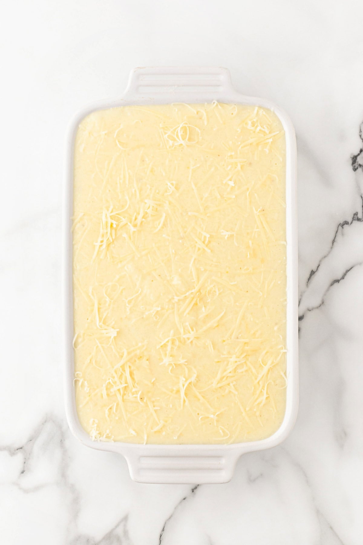 Grits casserole mixture topped with shredded cheese in a baking dish