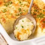 Spoonful of creamy baked grits casserole lifted from a white baking dish with a golden cheesy top and parsley