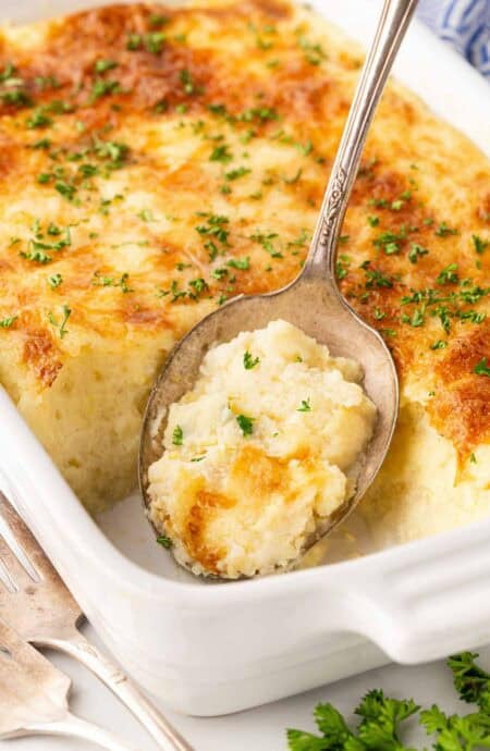 Spoonful of creamy baked grits casserole lifted from a white baking dish with a golden cheesy top and parsley