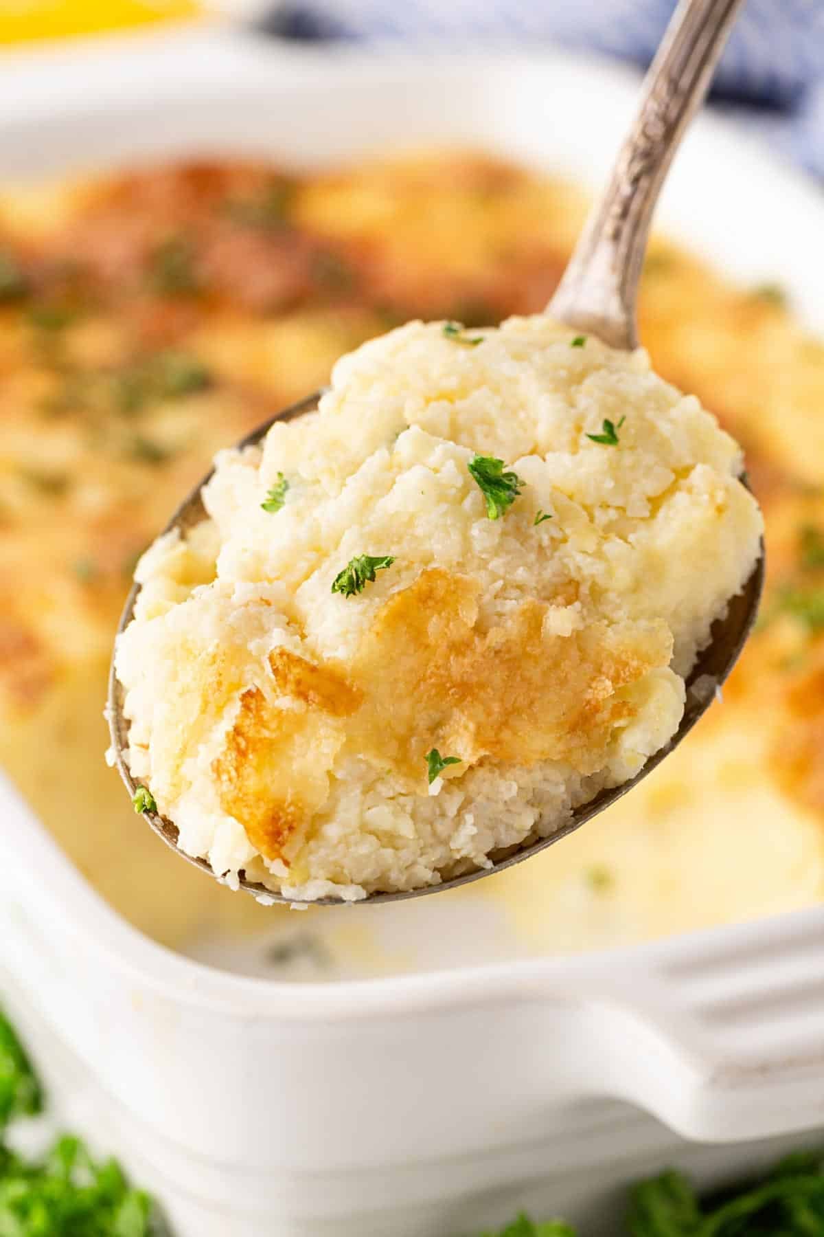 Closeup of creamy baked grits casserole with a golden cheese crust and parsley on a serving spoon