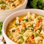 Two bowls of creamy chicken noodle soup garnished with fresh parsley on a countertop