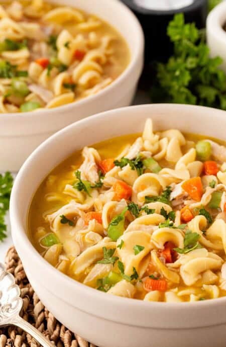 Two bowls of creamy chicken noodle soup garnished with fresh parsley on a countertop