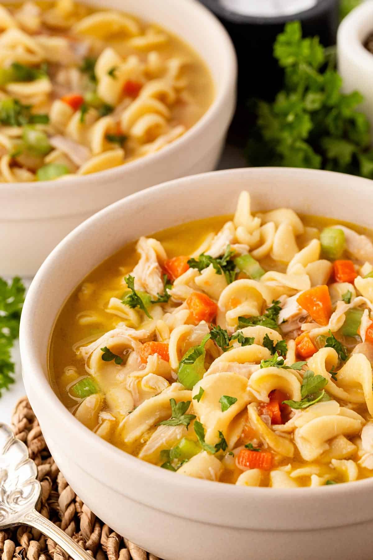 Two bowls of creamy chicken noodle soup garnished with fresh parsley on a countertop