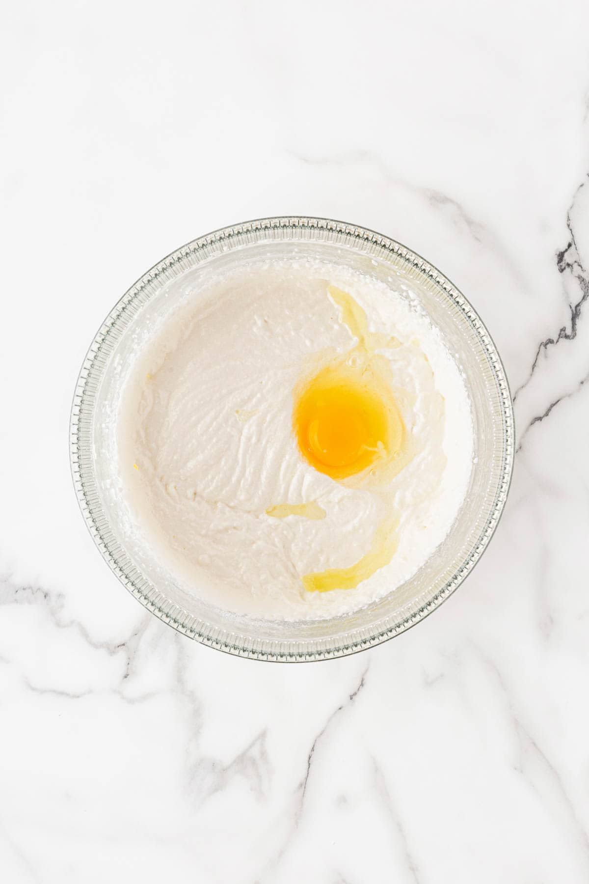A glass bowl filled with creamy cake batter and a cracked egg on top