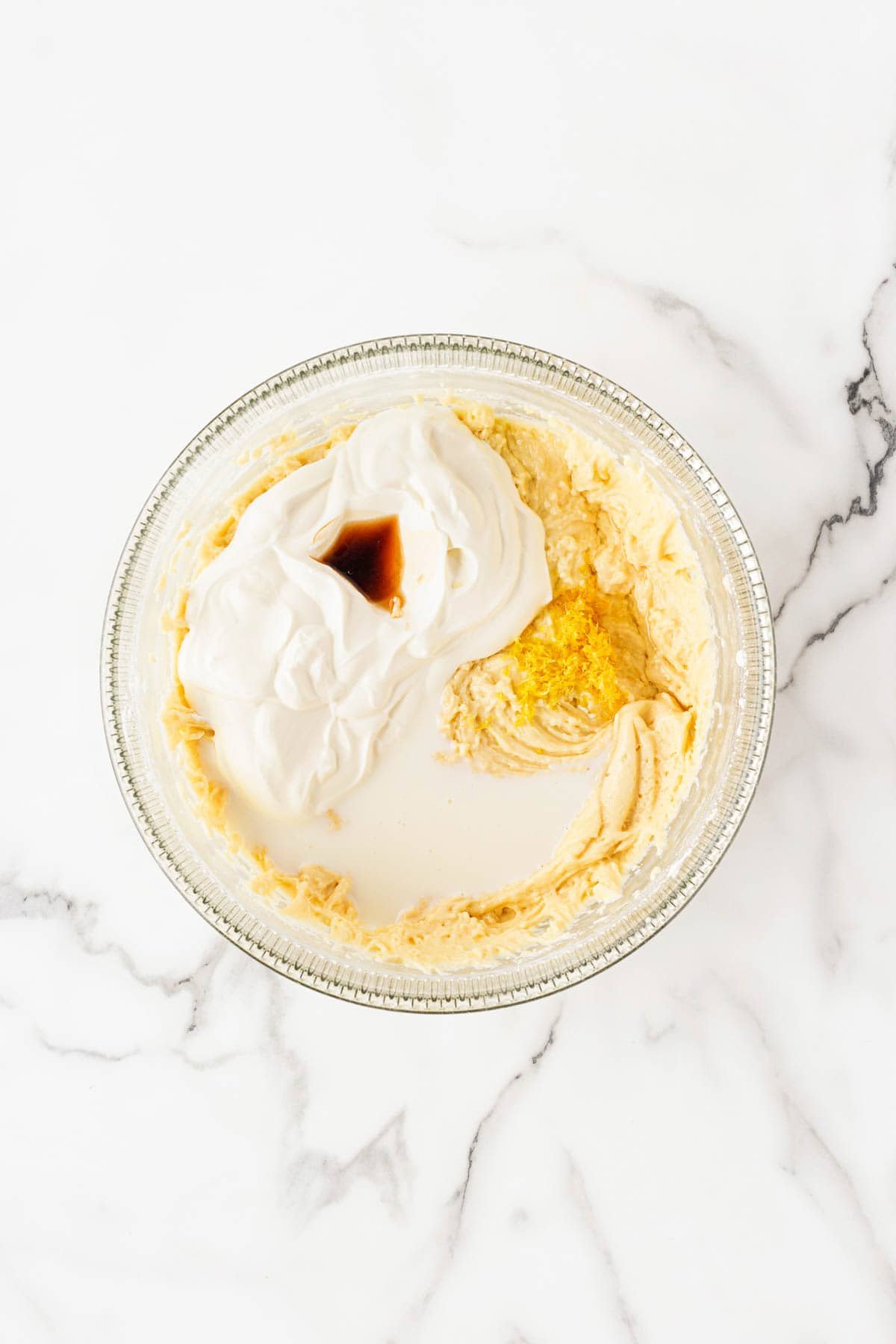 A mixing bowl with batter, milk, sour cream, lemon and vanilla extracts, and lemon zest being added