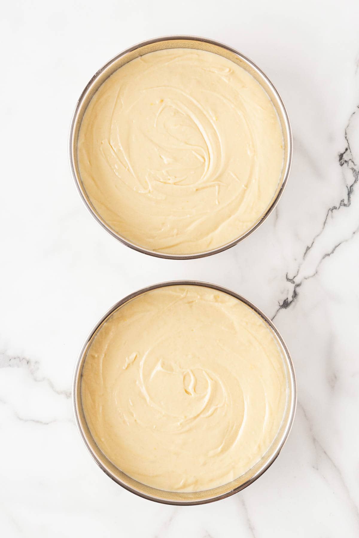 Two round baking pans filled with smooth lemon cake batter, ready to bake
