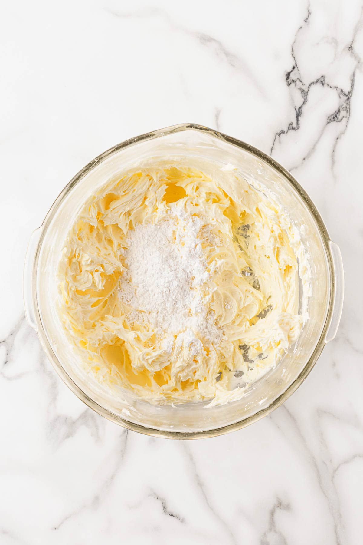 A mixing bowl with whipped cream cheese and powdered sugar being combined