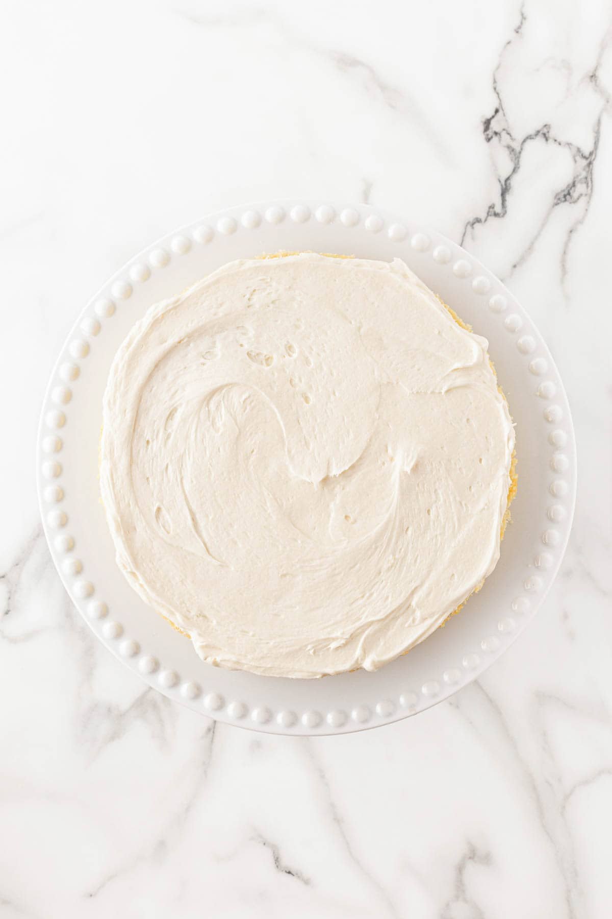 A single lemon cake layer topped with a smooth layer of frosting on a white plate