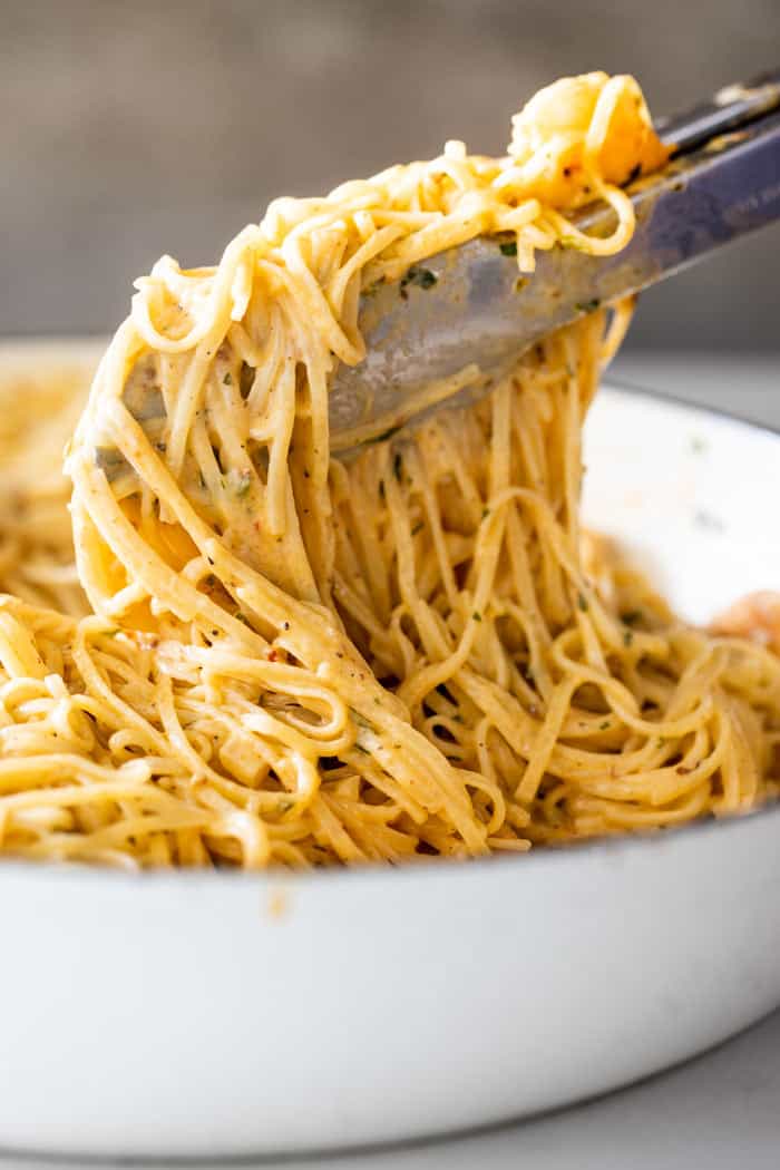 Linguine pasta with cream sauce being lifted from pot to place on plate