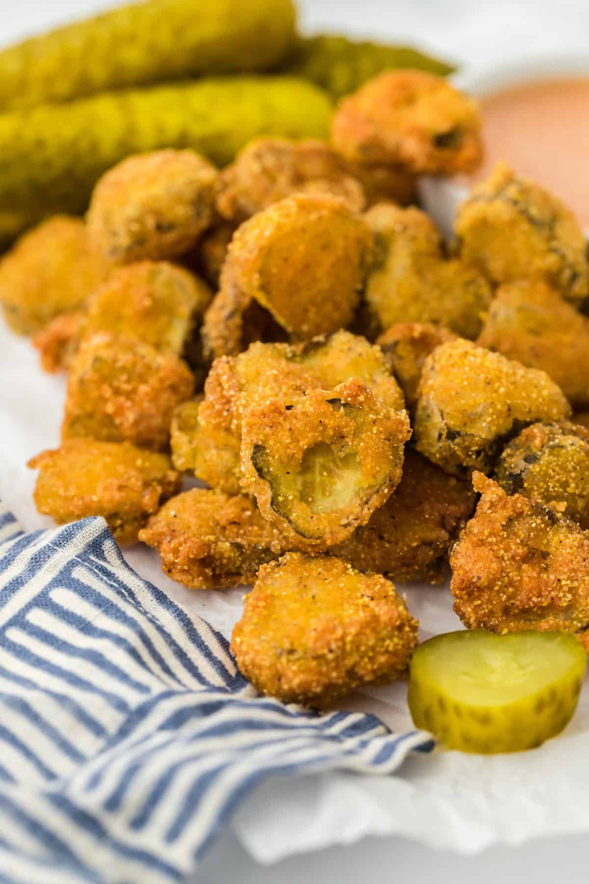 A fried pickles recipe against white background with striped napkin and whole dill pickles in the background