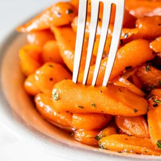 A close up of honey glazed carrots with fork pierced into one carrot