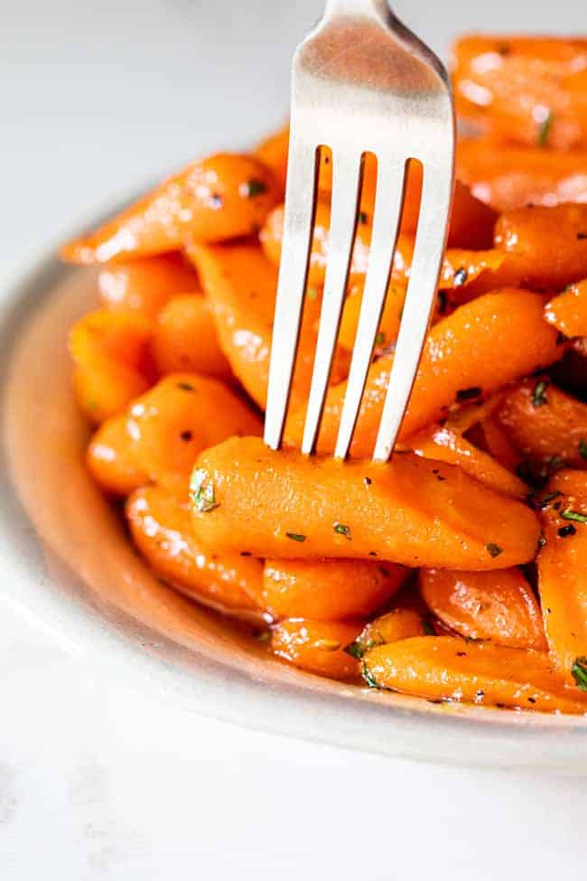 A close up of honey glazed carrots with fork pierced into one carrot