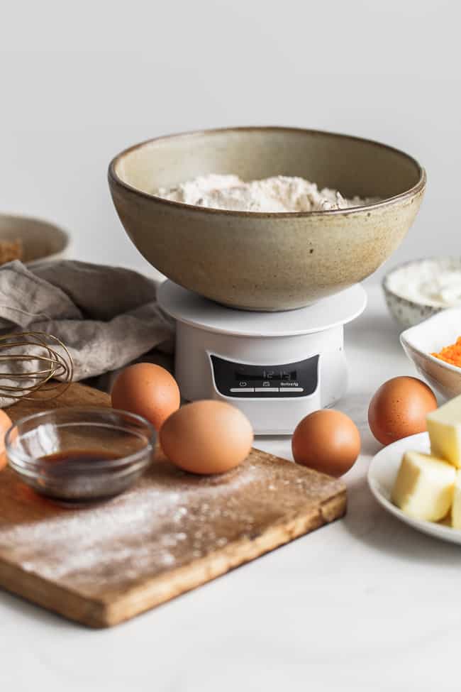 Ingredients to bake with including a bowl of flour, eggs, vanilla and butter set up