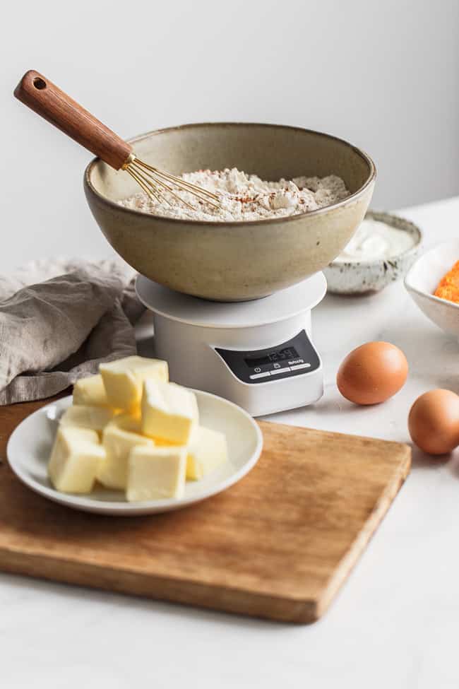 A bowl of cake flour surrounded by butter, eggs and sugar ready to bake with