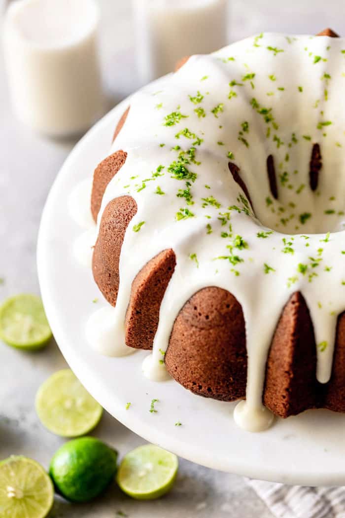 A close up of full key lime cake with cream cheese glaze and lime zest garnish ready to serve on cake platter
