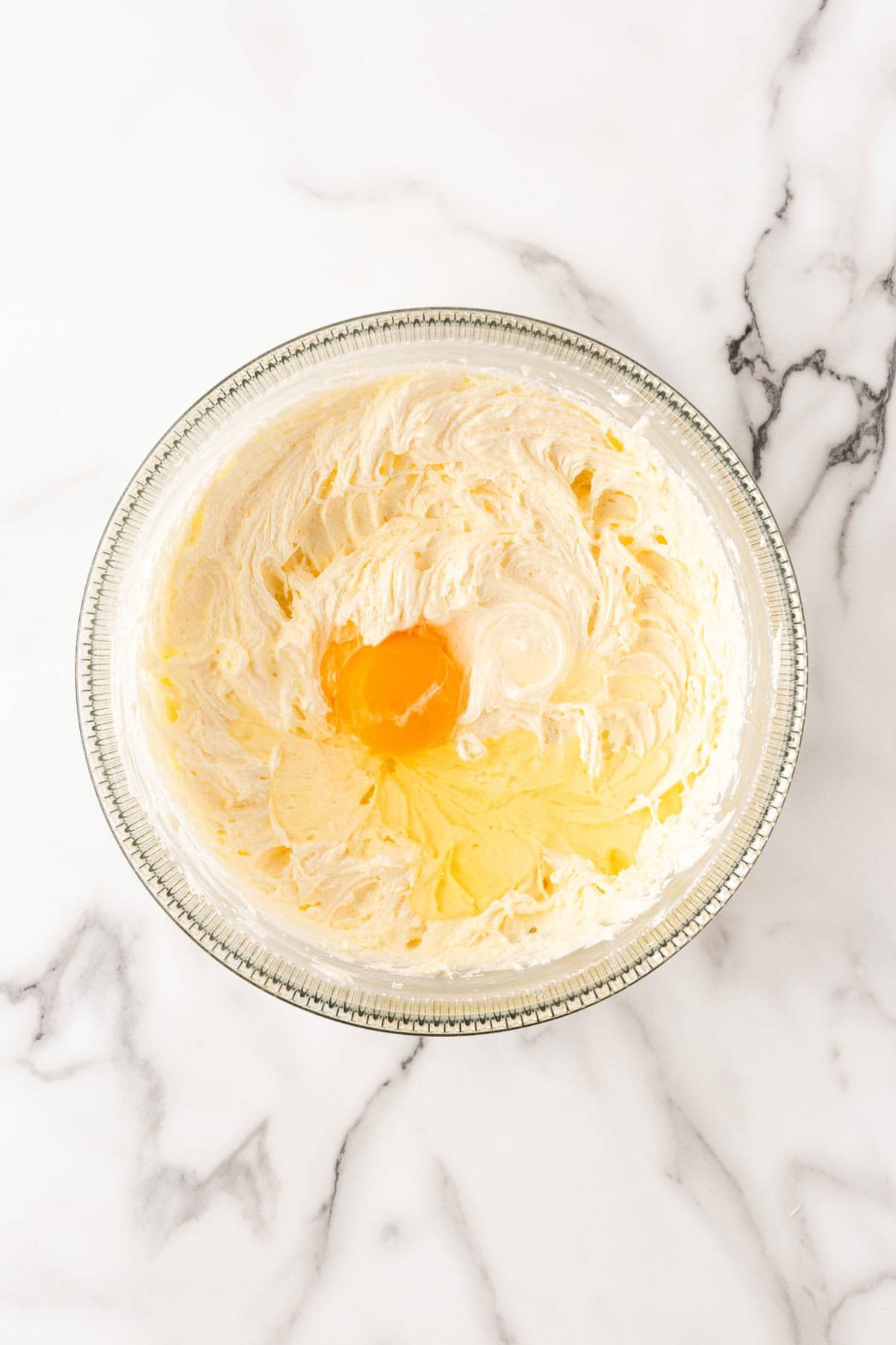 Overhead view of creamed butter, shortening, cream cheese, and sugar in a bowl with a whole egg added in the center