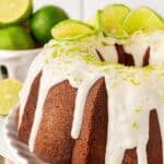 Closeup of a key lime cake topped with white glaze, lime zest, and sliced limes on a serving platter