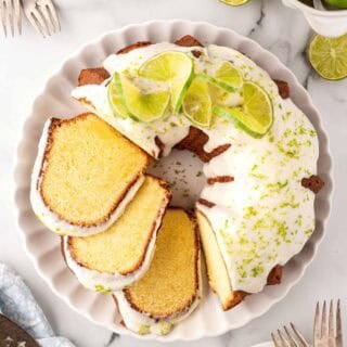 Overhead shot of key lime Bundt cake topped with white glaze, lime zest, and sliced limes on a serving platter