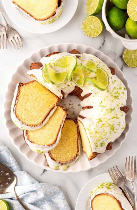 Overhead shot of key lime Bundt cake topped with white glaze, lime zest, and sliced limes on a serving platter