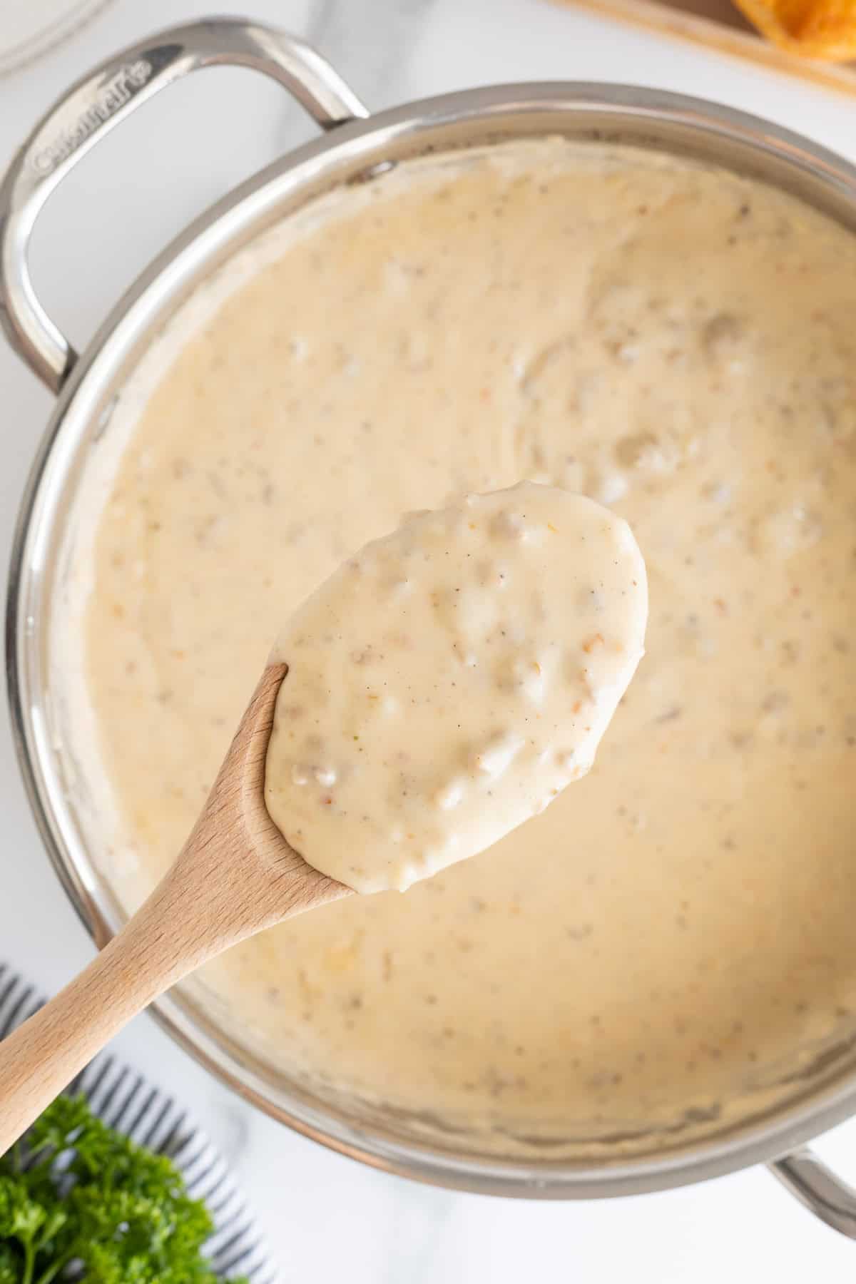 A wooden spoon lifting a thick scoop of sawmill gravy from a saucepan
