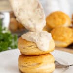Spoonful of sawmill gravy being poured over stacked golden biscuits on a plate