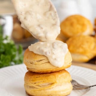 Spoonful of sawmill gravy being poured over stacked golden biscuits on a plate