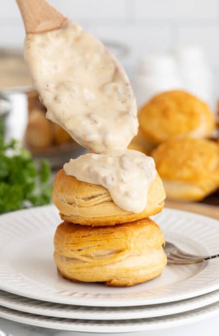 Spoonful of sawmill gravy being poured over stacked golden biscuits on a plate