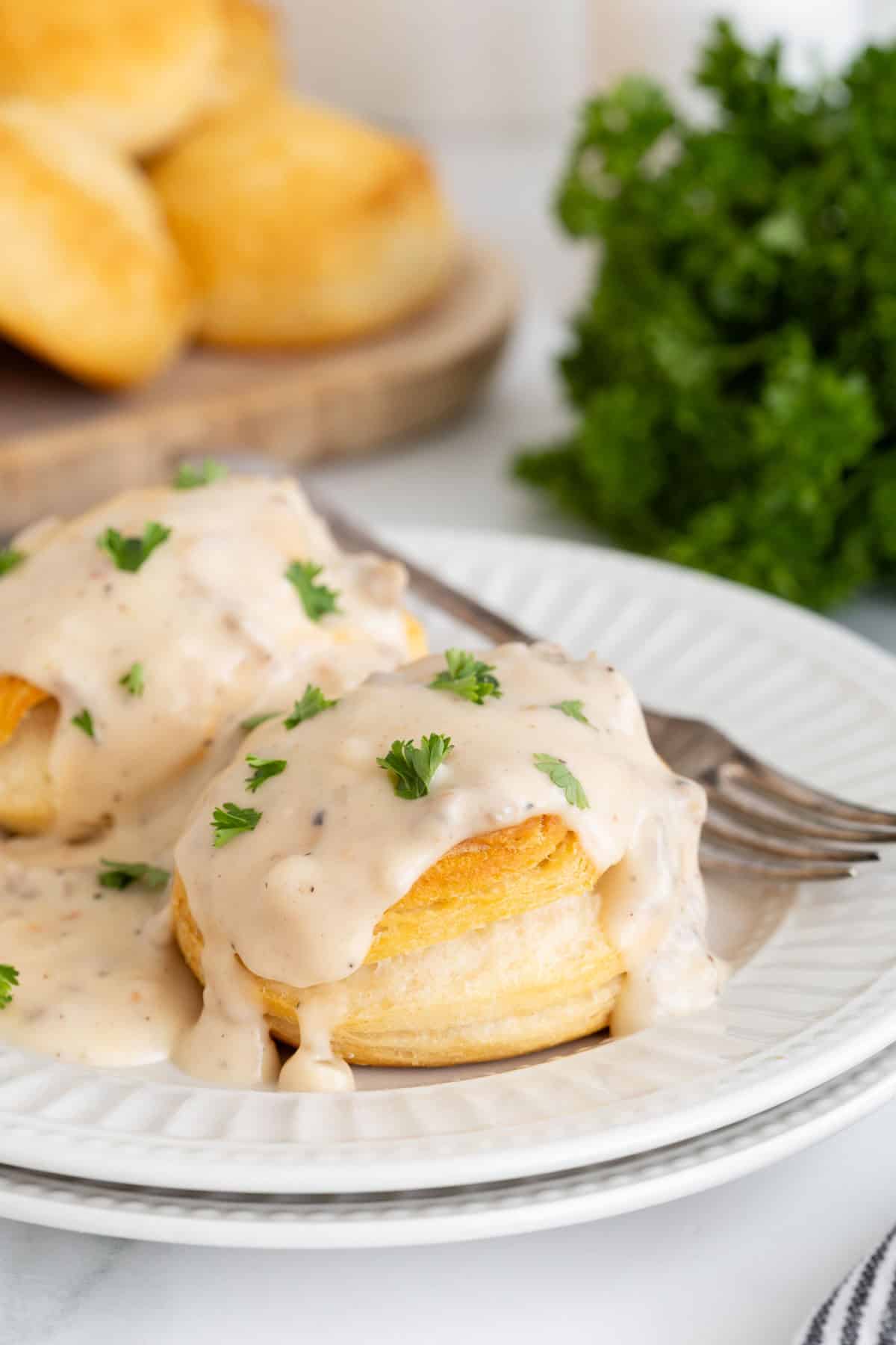 Closeup of biscuits with sawmill gravy garnished with parsley, with more biscuits in the background