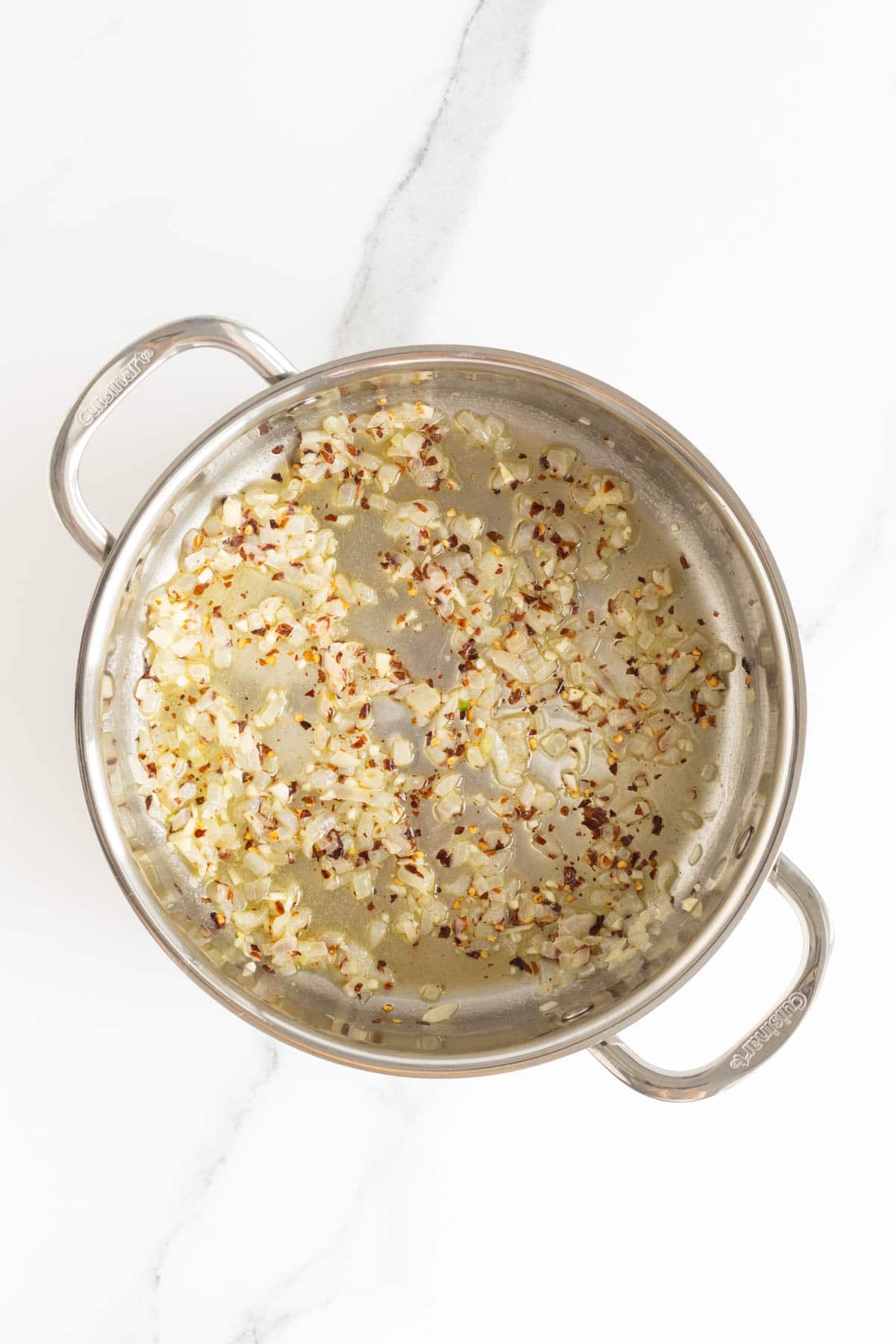 Golden sautéed onion mixture with red pepper flakes in a stainless steel pan