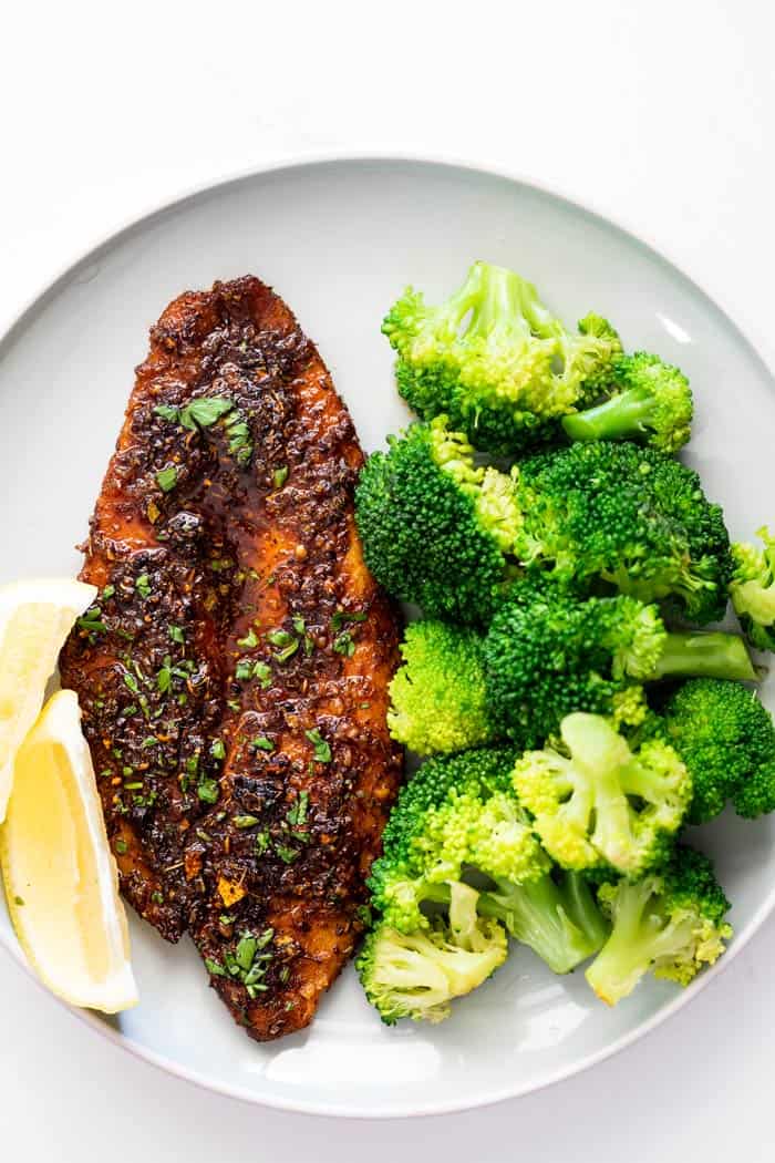 Blackened catfish fillet on plate with lemons and fresh broccoli