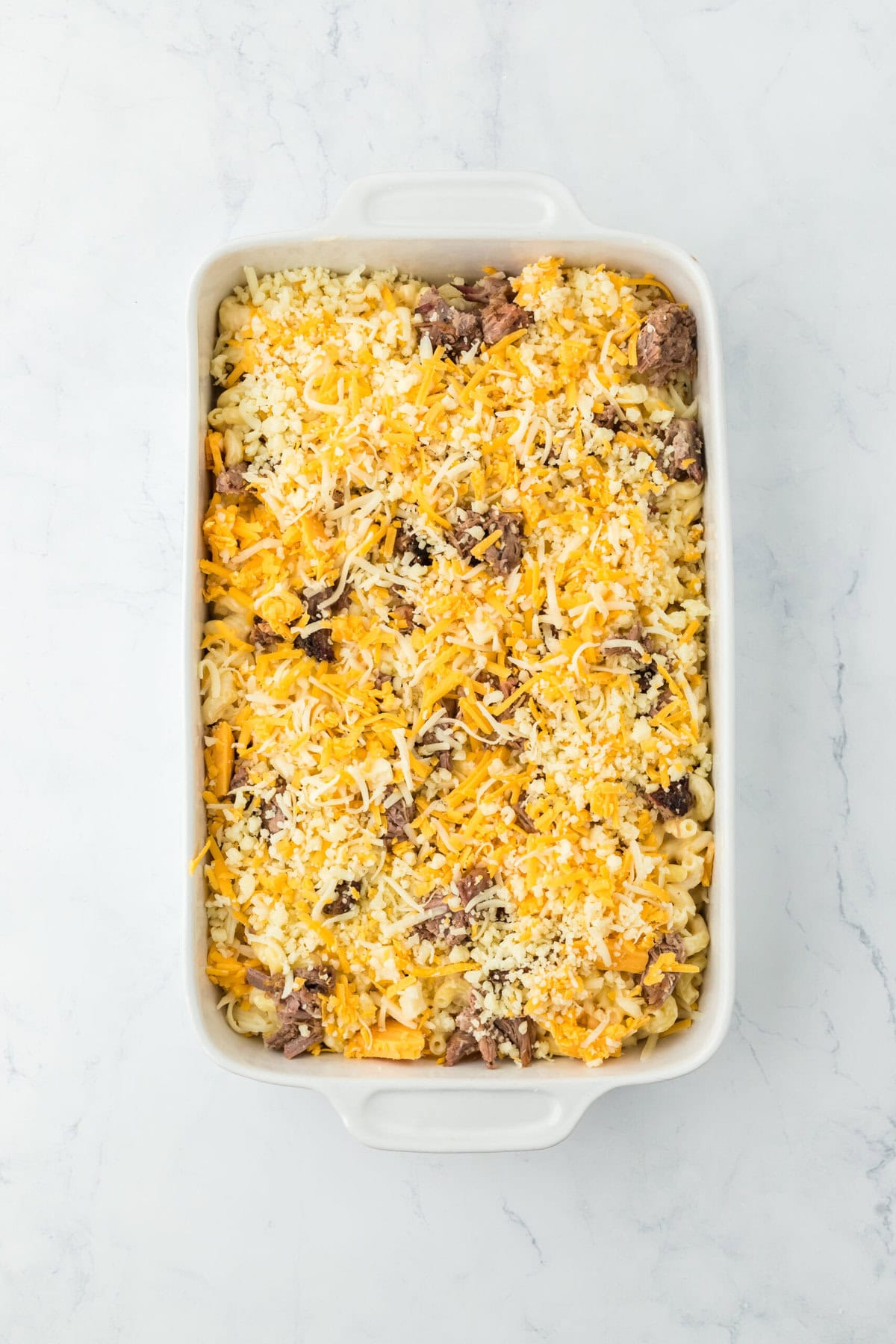 Cheese and brisket filled mac in a white casserole dish before baking on white countertop