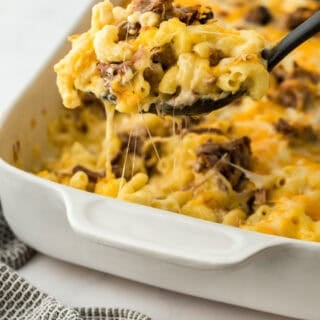 Beef brisket mac and cheese being lifted from a white casserole dish to serve