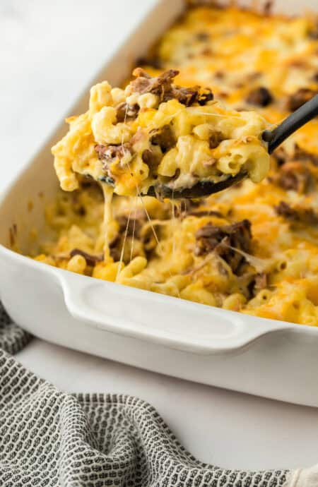 Beef brisket mac and cheese being lifted from a white casserole dish to serve